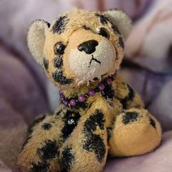 a cheetah plush with a bracelet with purple and black beads and a witch cat charm around its neck