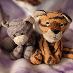 A gray tabyy cat plush and a tiger plush sitting side by side.